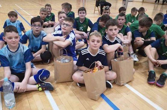 Zdjęcie grupowe. Zawodnicy i  zawodniczki siedzą na parkiecie. Na pierwszym planie zawodnicy z UKS Libero-Łebień.