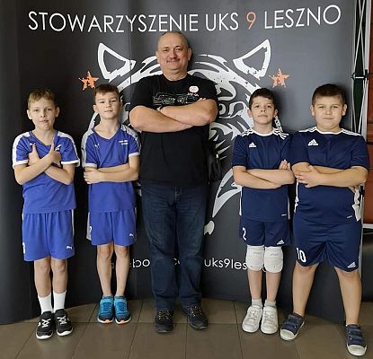 Dwie dwójki chłopców pozują do zdjęcia, w środku z trenerem.