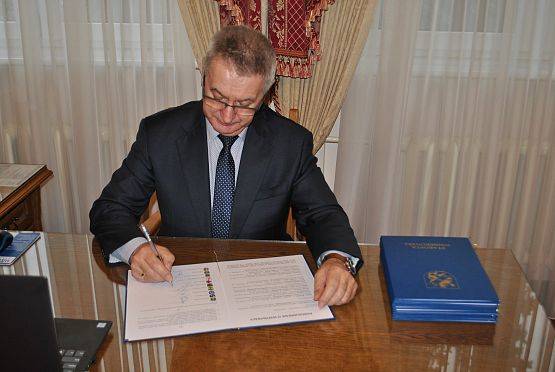 Wójt gminy, przy biurku w swoim gabinecie, podpisuje porozumienie.