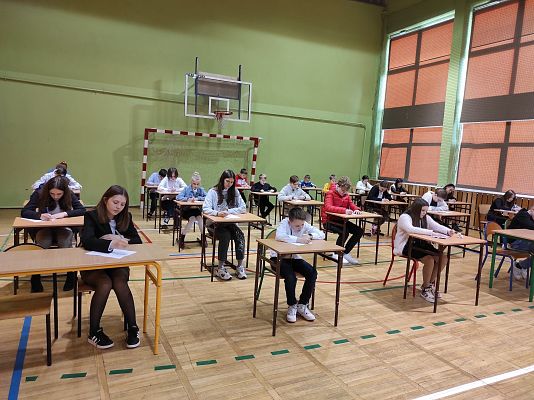 W sali sportowej, w ławkach, uczniowie piszą test z zakresu wiedzy pożarniczej.