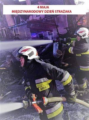 Dwaj strażacy podczas akcji gaszenia pożaru budynku mieszkalnego. grafika