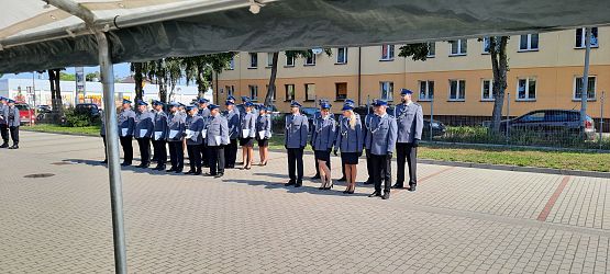 Odznaczeni policjanci stoją w szeregu na placu przed budynkiem komendy.