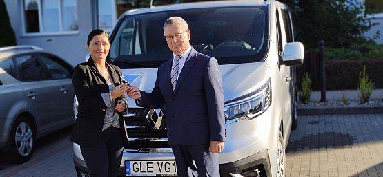 Wójt Gminy na tle nowego samochodu przekazuje kluczyki kierownik GOPS. grafika
